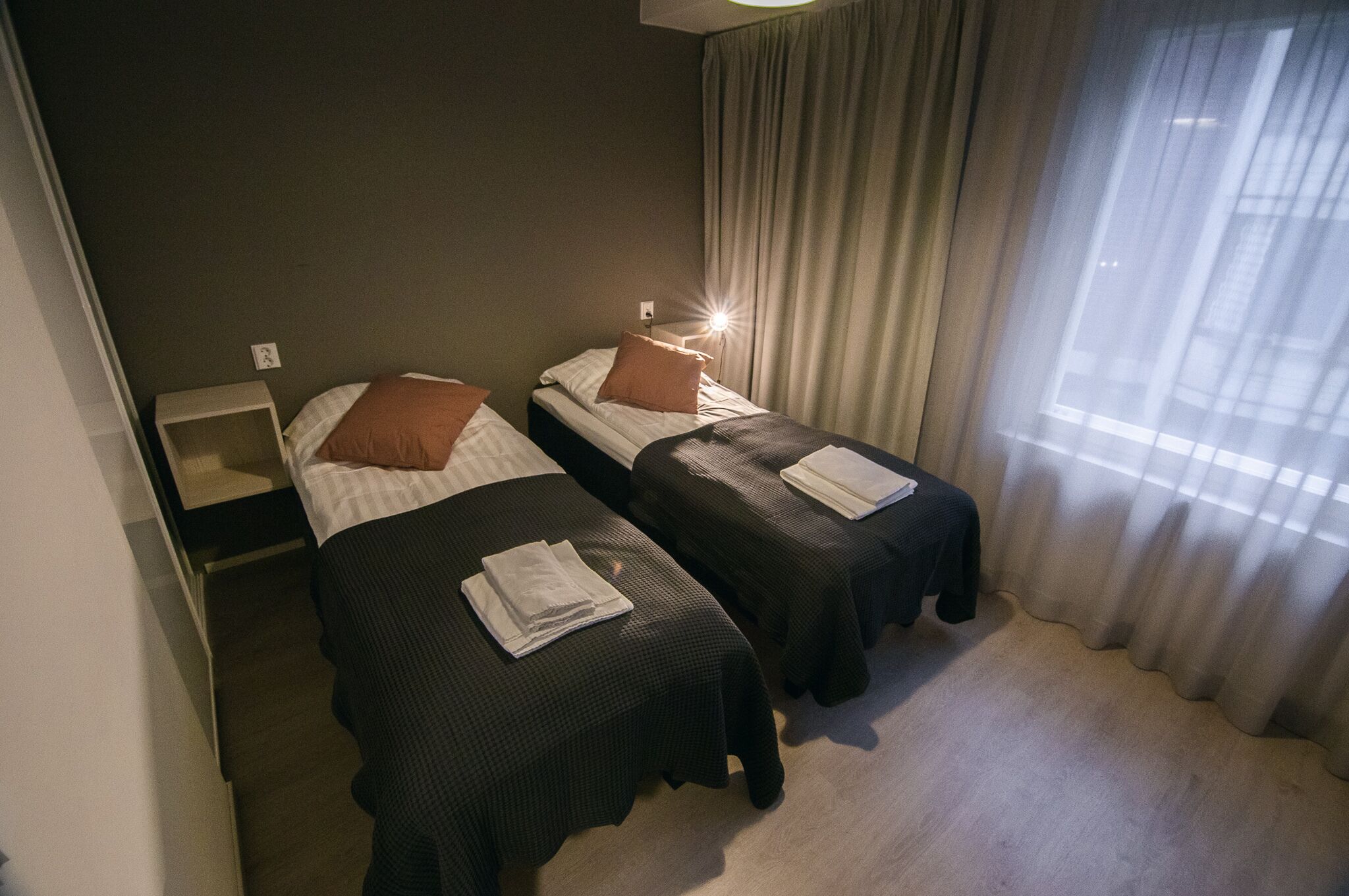 Una habitación de hotel con dos camas individuales, una mesita de noche y una ventana con cortinas.