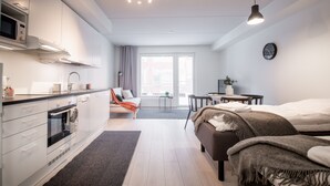 A modern, well-lit room with a kitchenette, a bed, a desk, and a view of the outside. - Spot Apartments Espoon Keskus (Espoo)