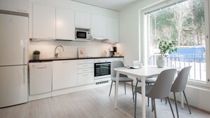 A modern kitchen with white cabinetry, a built-in microwave, and a dining area with a white table and grey chairs. - Spot Apartments Espoon Keskus (Espoo)
