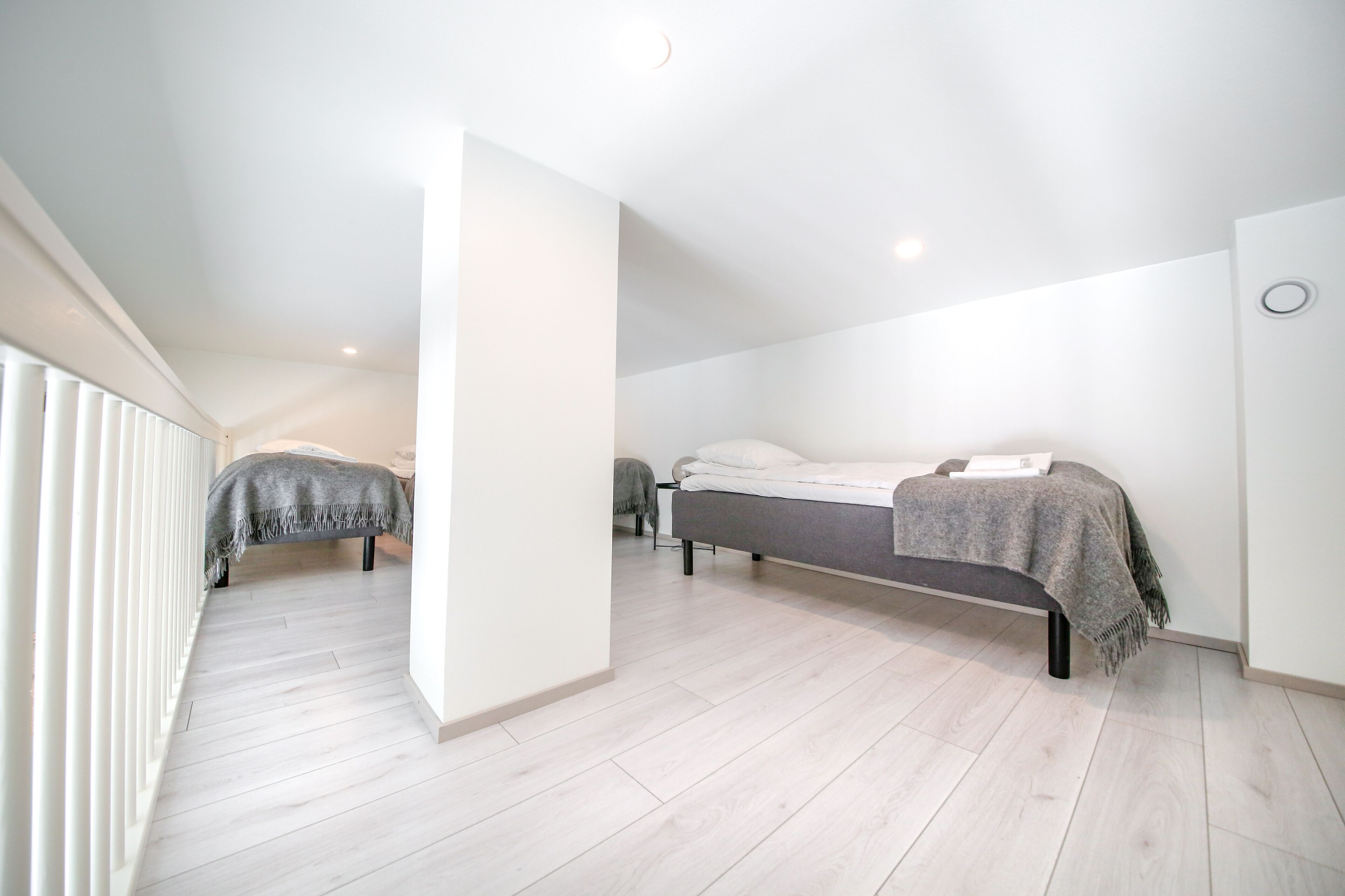A modern, minimalist bedroom with a large bed, a smaller bed, and a bench.