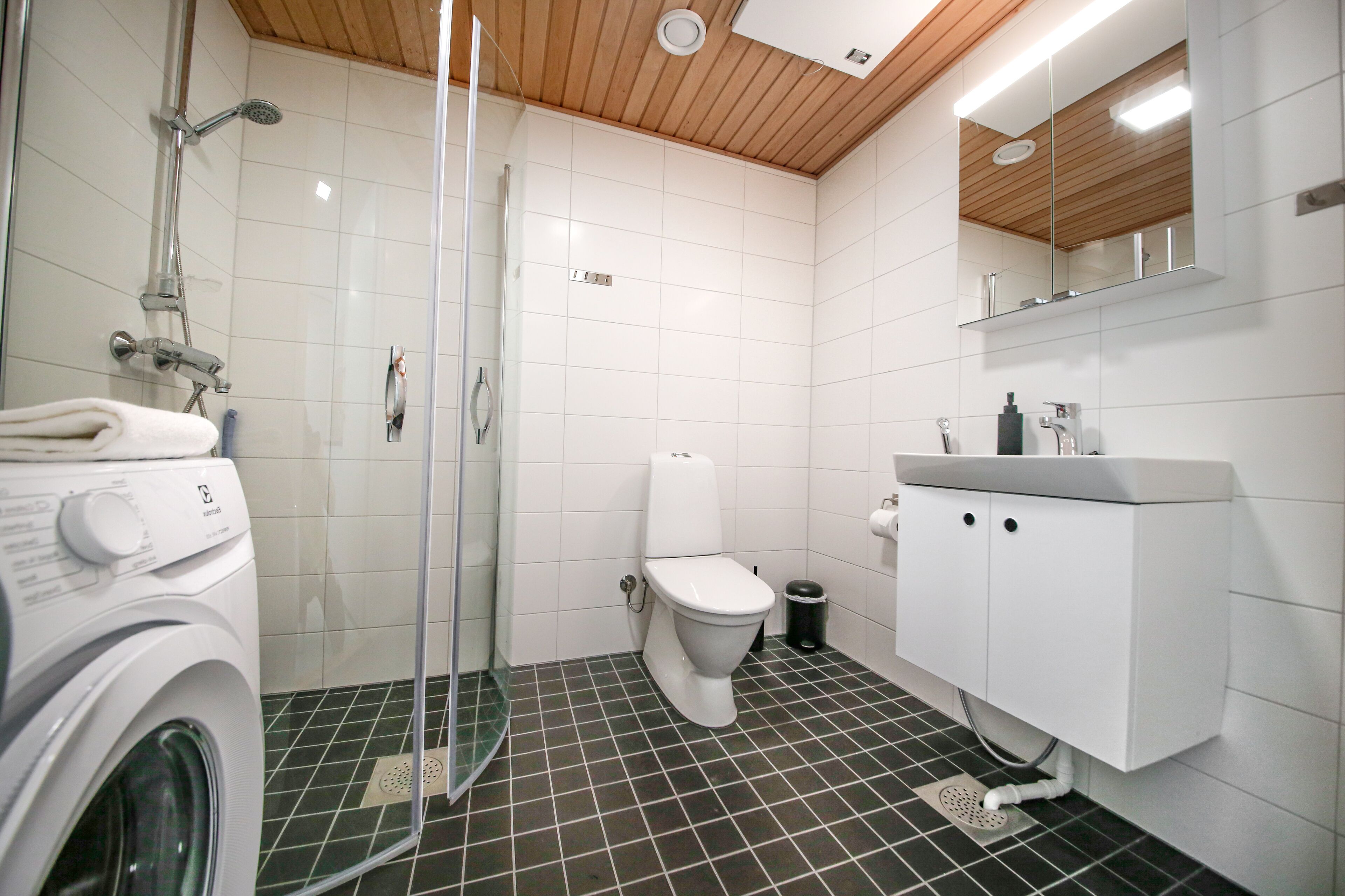 Een moderne badkamer met een douchecabine van glas, een wit toilet en een inbouw wasmachine.