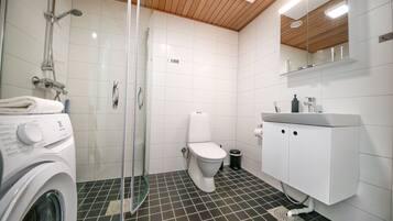 Een moderne badkamer met een douchecabine van glas, een wit toilet en een inbouw wasmachine.