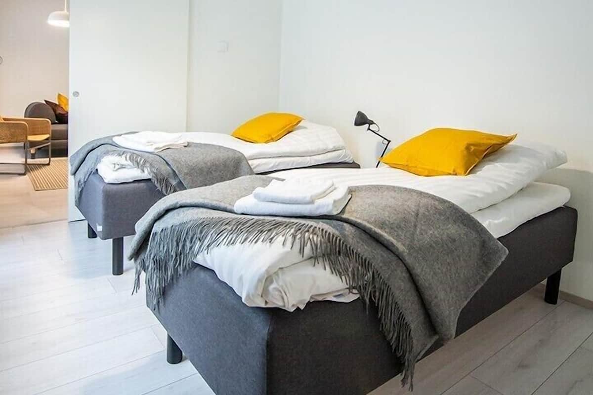 Camera da letto moderna con due letti, ognuno con una testiera grigia e biancheria da letto bianca, impreziosita da cuscini gialli.