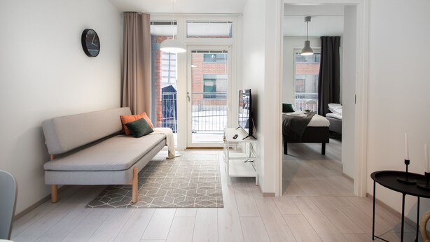 A modern living room with a sofa, a TV, and a dining area. - Spot Apartments Espoon Keskus (Espoo)
