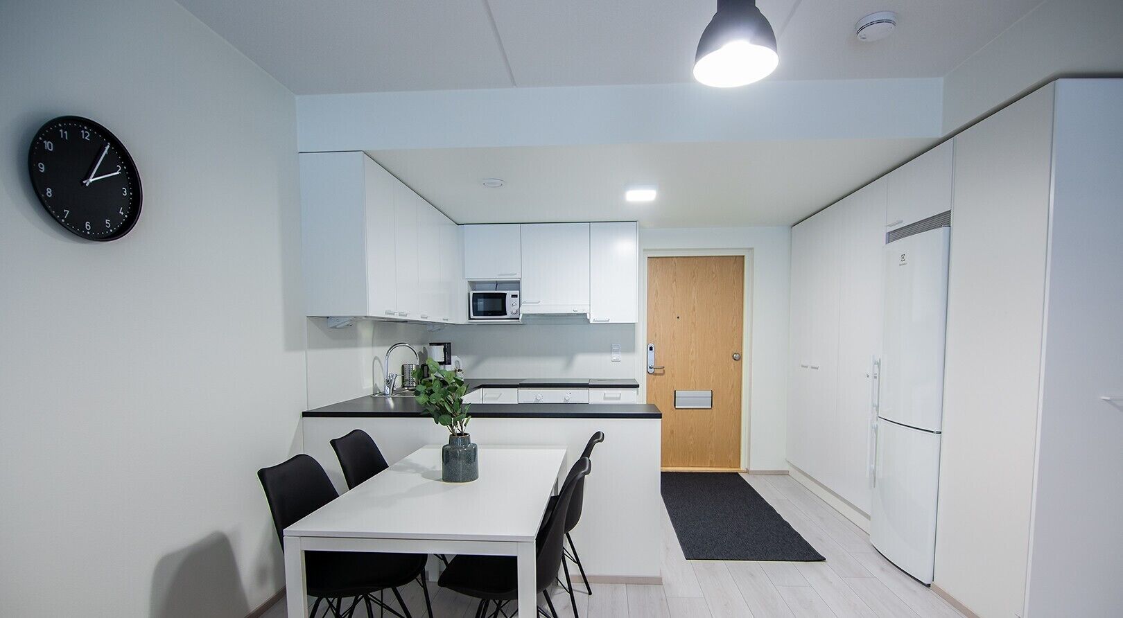 Een moderne keuken met witte kasten, een magnetron, en een eethoek met een tafel en stoelen.