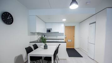 Een moderne keuken met witte kasten, een magnetron, en een eethoek met een tafel en stoelen.