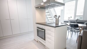 A modern kitchen with white cabinetry, a built-in oven, and a dining area with a gray sofa and chairs. - Spot Apartments Espoon Keskus (Espoo)
