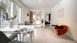 A modern, well-lit living area with a dining table, chairs, a sofa, and a red armchair. There is a potted plant on the dining table and a flat-screen TV on a stand. - Spot Apartments Espoon Keskus (Espoo)