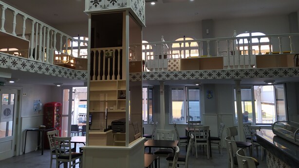 A spacious indoor area with multiple seating arrangements, a central column with shelves, and a mezzanine level with a balcony. - Hotel Aros (Casas-Ibanez)