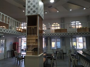 Un vaste espace intérieur aménagé avec de nombreux coins salon, une colonne centrale dotée d’étagères et une mezzanine avec balcon.