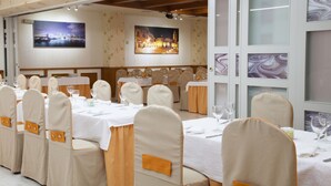 A banquet hall with tables set for a formal event, featuring white tablecloths and matching chairs with orange sashes. - Hotel Aros (Casas-Ibanez)