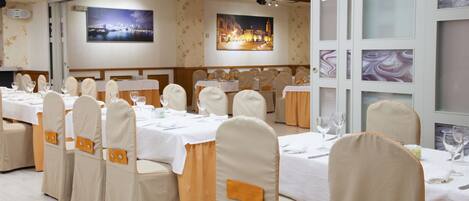 Un salón de banquetes con mesas dispuestas para un evento formal, con manteles blancos y sillas a juego adornadas con cintas naranjas.