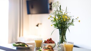 A breakfast setting with a sandwich, bowl of strawberries, a vase of flowers, and glasses of orange juice on a table.