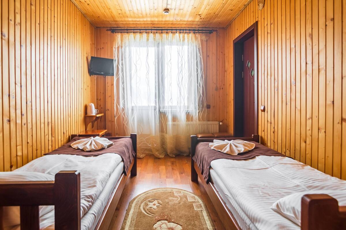 Ein Holzhütten-Zimmer mit zwei Betten, einem Fernseher und einem Fenster mit Vorhängen.
