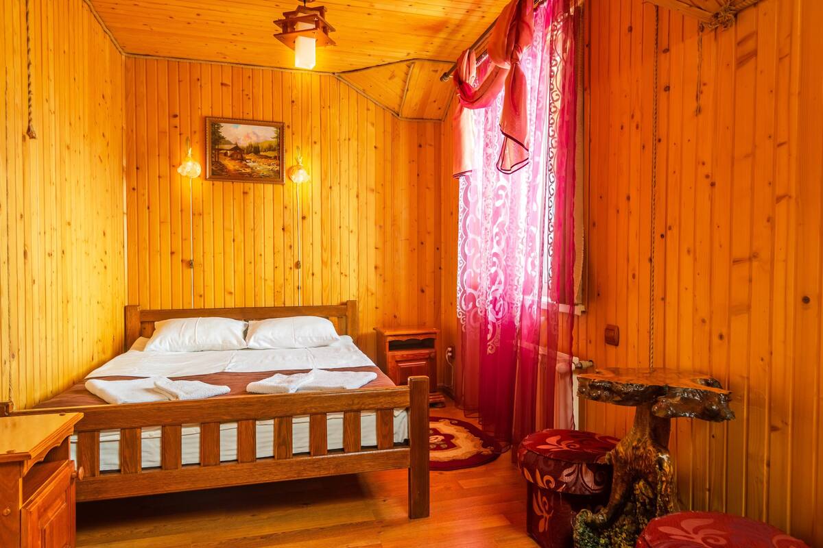 Ein Zimmer mit Holzboden, einem Bett, einem Nachttisch, einer Lampe und einem Gemälde an der Wand.