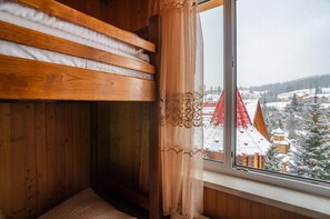 A wooden room with a bunk bed and a window overlooking a snowy village. - Villa Milena (Bukovel)