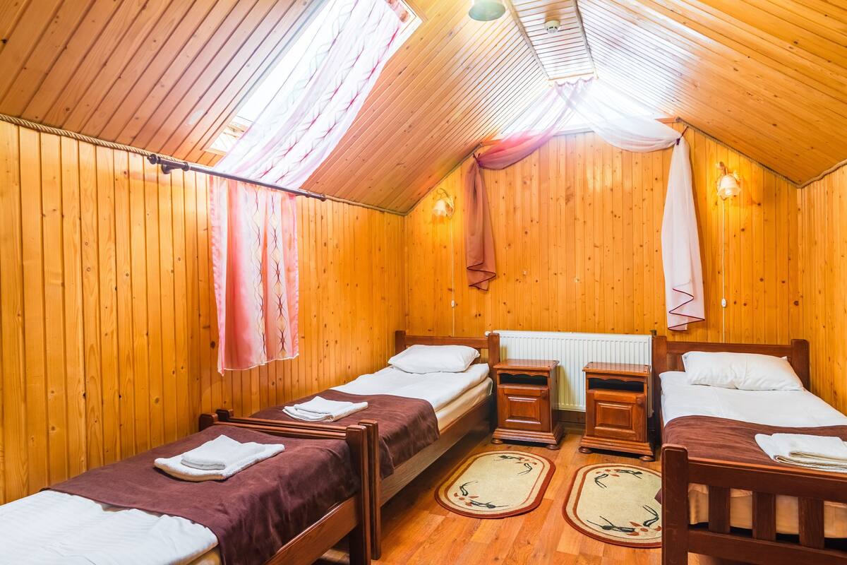 Ein Holzhütten-Zimmer mit zwei Betten, einem kleinen Tisch und einem Fenster mit Vorhängen.