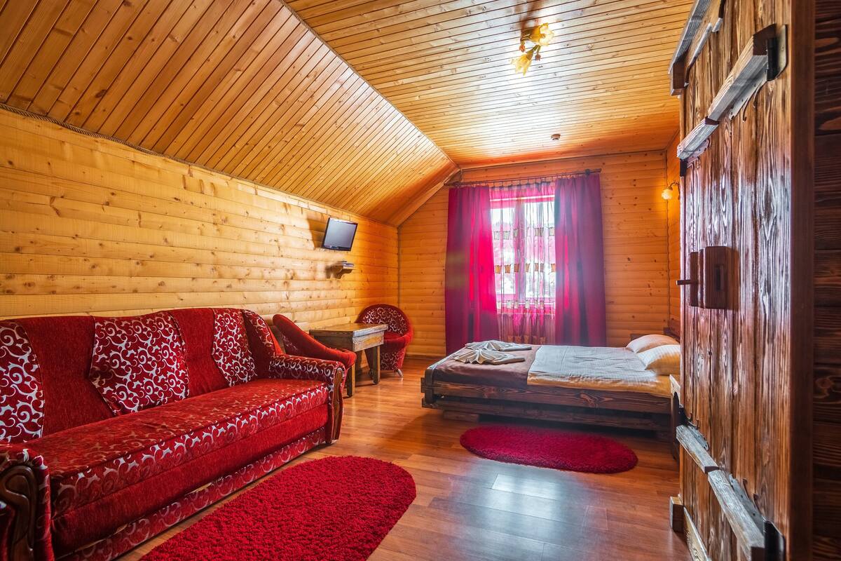 Ein gemütliches Blockhaus-Zimmer mit Holzboden, einem roten Sofa, einem Bett und einem kleinen Tisch mit Stuhl.