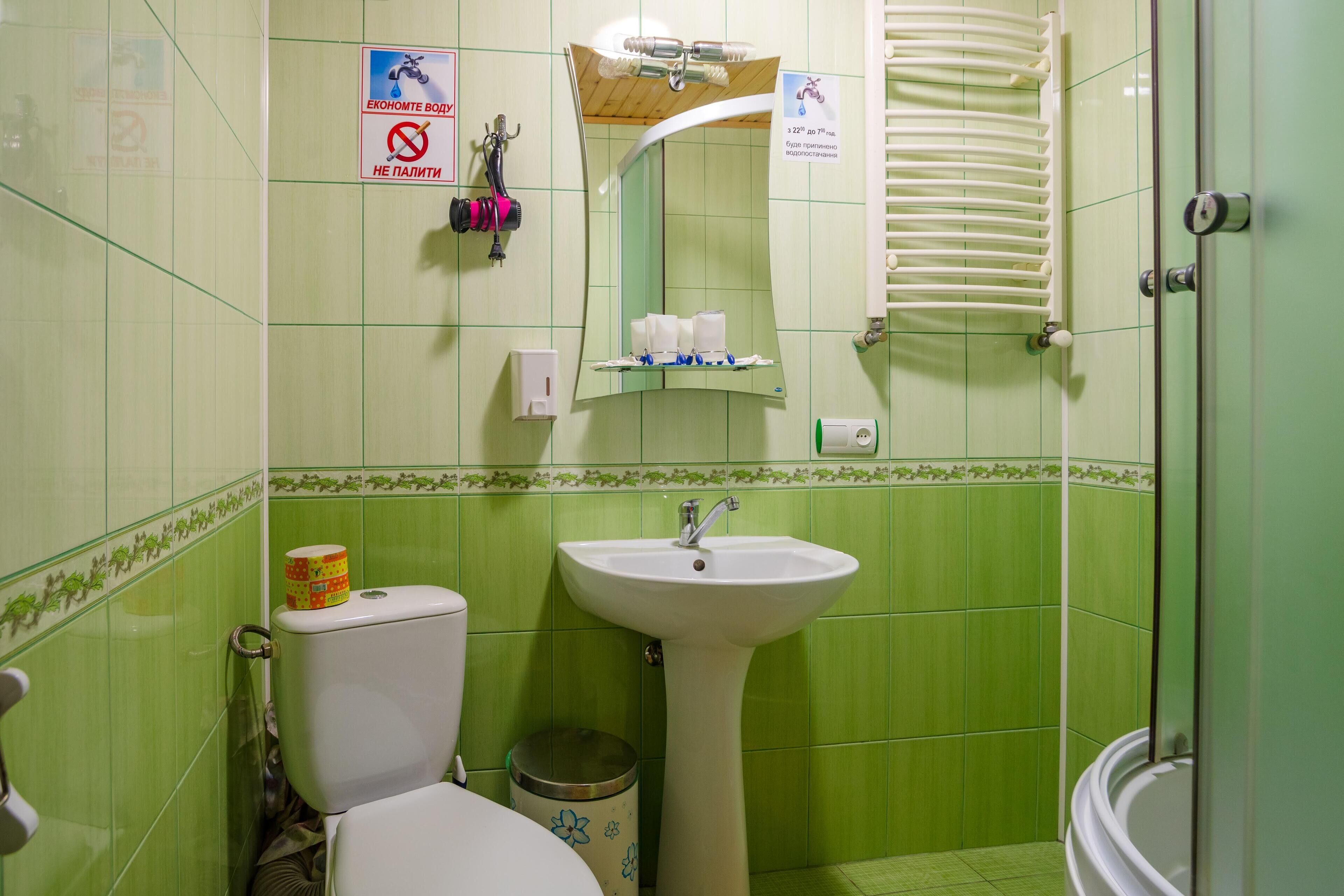 Baño con azulejos verdes, un lavabo blanco, inodoro y ducha.