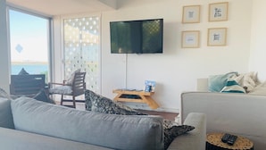 Een woonkamer met een bank, een stoel, een bijzettafeltje met een boek, en een tv aan de muur.