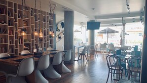 Een ruim café met houten tafels en witte stoelen, omringd door boekenkasten en hangende lampen.