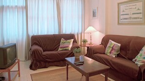 Ein Wohnzimmer mit zwei braunen Sofas, einem kleinen Tisch, einem Fernseher auf einem Schrank und einer Lampe auf einem Beistelltisch.