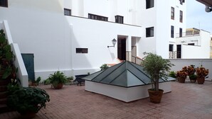 Ein Innenhof mit einem zentral platzierten Blumentopf, einer kleinen Sitzecke und einem Gebäude mit mehreren Fenstern und Balkonen.