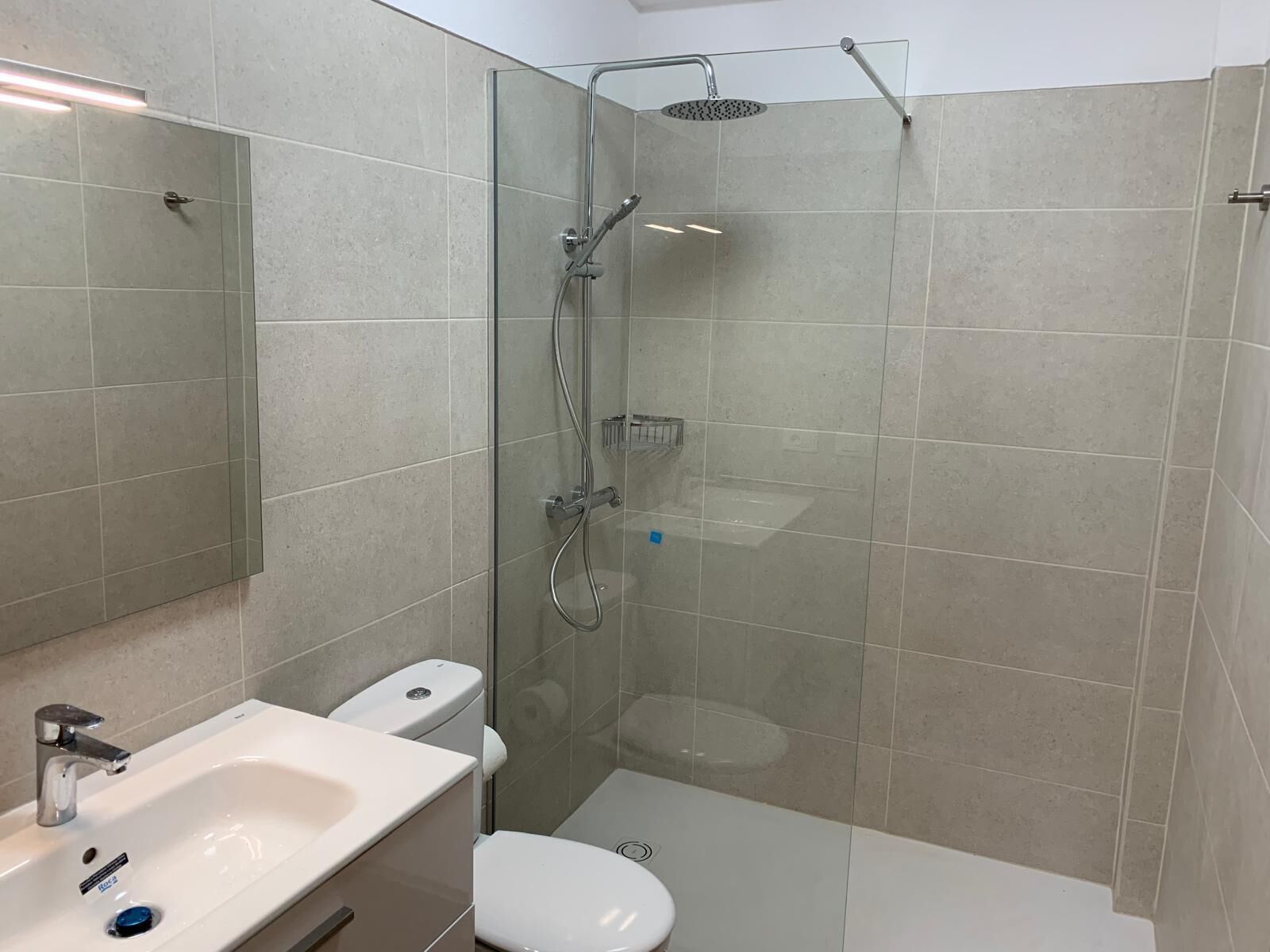 Ein modernes Badezimmer mit einer Duschkabine, einem weißen Waschbecken und einer Toilette.