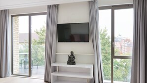 Ein modernes Wohnzimmer mit einem Flachbildfernseher an einer weißen Wandhalterung, einer Statue und einer Schiebetür zu einem Außenbereich.