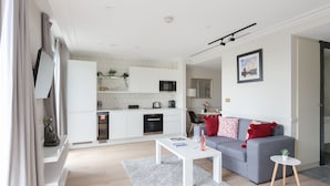 Ein modernes Wohnzimmer mit grauem Sofa, weißem Couchtisch und einem kleinen runden Tisch mit Pflanze.