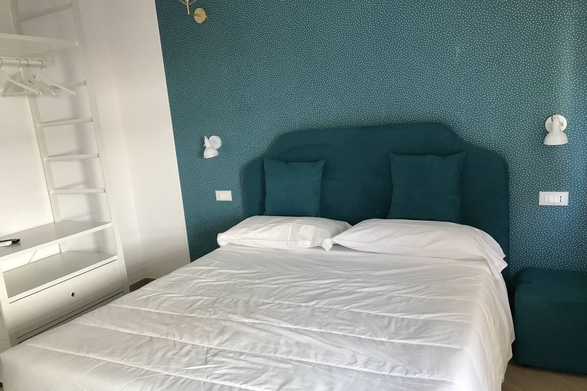 Une chambre avec un mur à pois turquoise, un lit blanc et une armoire blanche dotée d’une tringle pour suspendre les vêtements.