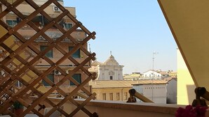 A terrace with a wooden lattice, potted plants, a white table, and a view of buildings in the background. - Affreschi Al Vaticano (Rome)
