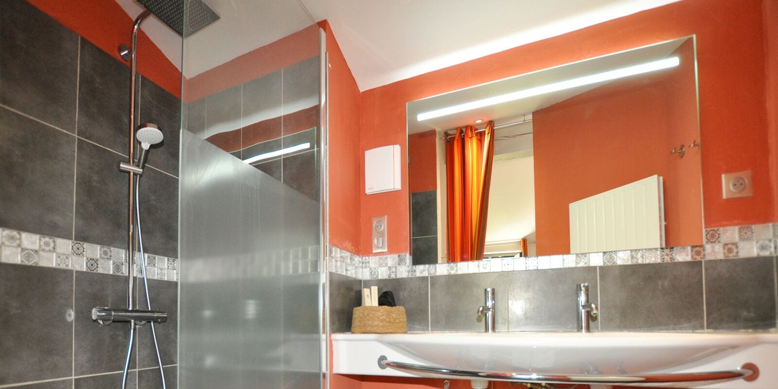 Een badkamer met een douche, wastafel en spiegel.