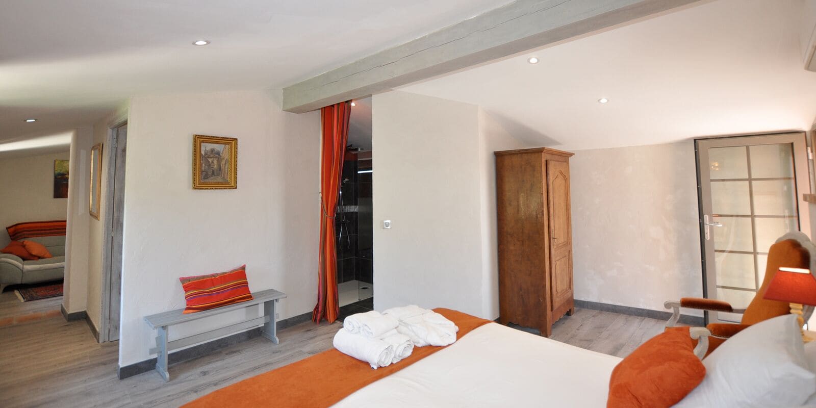 A hotel room with a bed, a bench, a wooden wardrobe, and a bathroom visible through an open door.