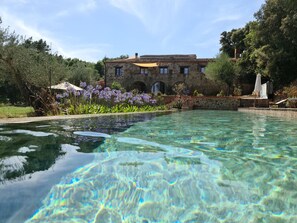 Uma piscina cristalina com um edifício de pedra ao fundo.