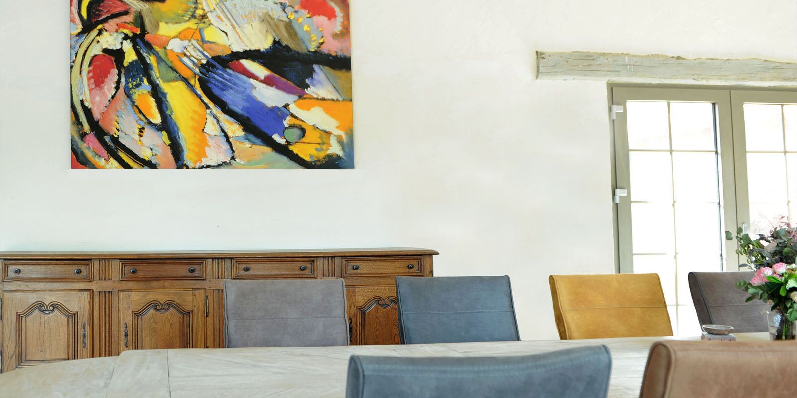 A bedroom with a bed, a wooden dresser, a painting, and a door with a window.