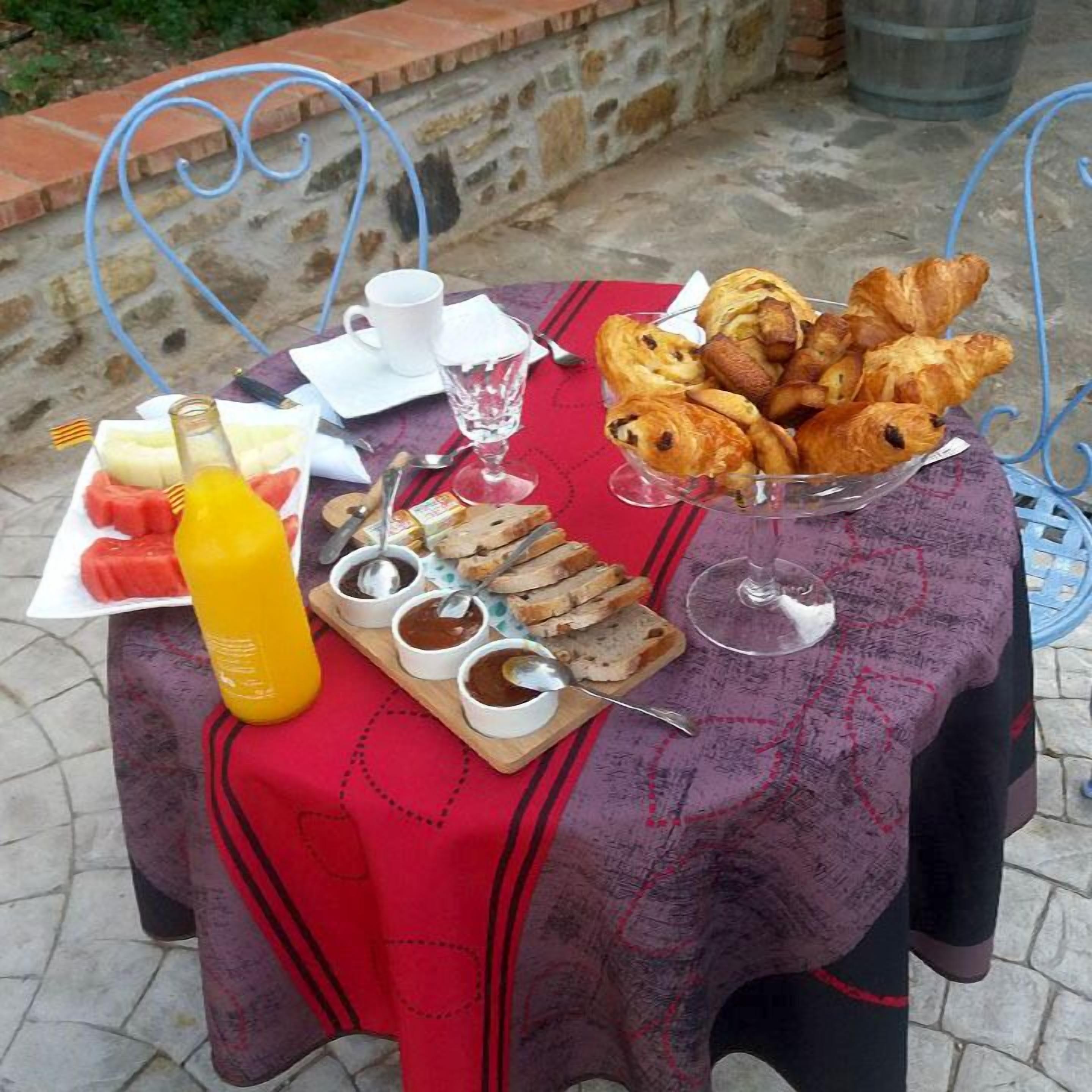 Una mesa dispuesta con cruasanes, pan, mermelada y una botella de zumo de naranja.