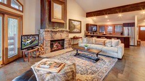 A spacious living room with a stone fireplace, a television, and a cozy seating area. - Deer Valley Enclave - Spacious 2BR, Mountain Views (Park City)