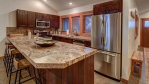 A kitchen with wooden cabinets, a stainless steel refrigerator, a granite countertop, and bar stools. - Deer Valley Enclave - Spacious 2BR, Mountain Views (Park City)