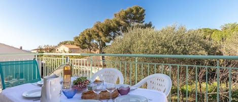 A table set outdoors with a white tablecloth, plates, cutlery, a bottle, glasses, and a loaf of bread.