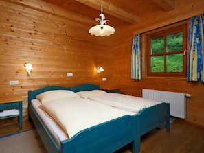 Un dormitorio de cabaña de madera con una cama doble, dos luces fijadas a la pared, un ventanal con cortinas y un radiador.