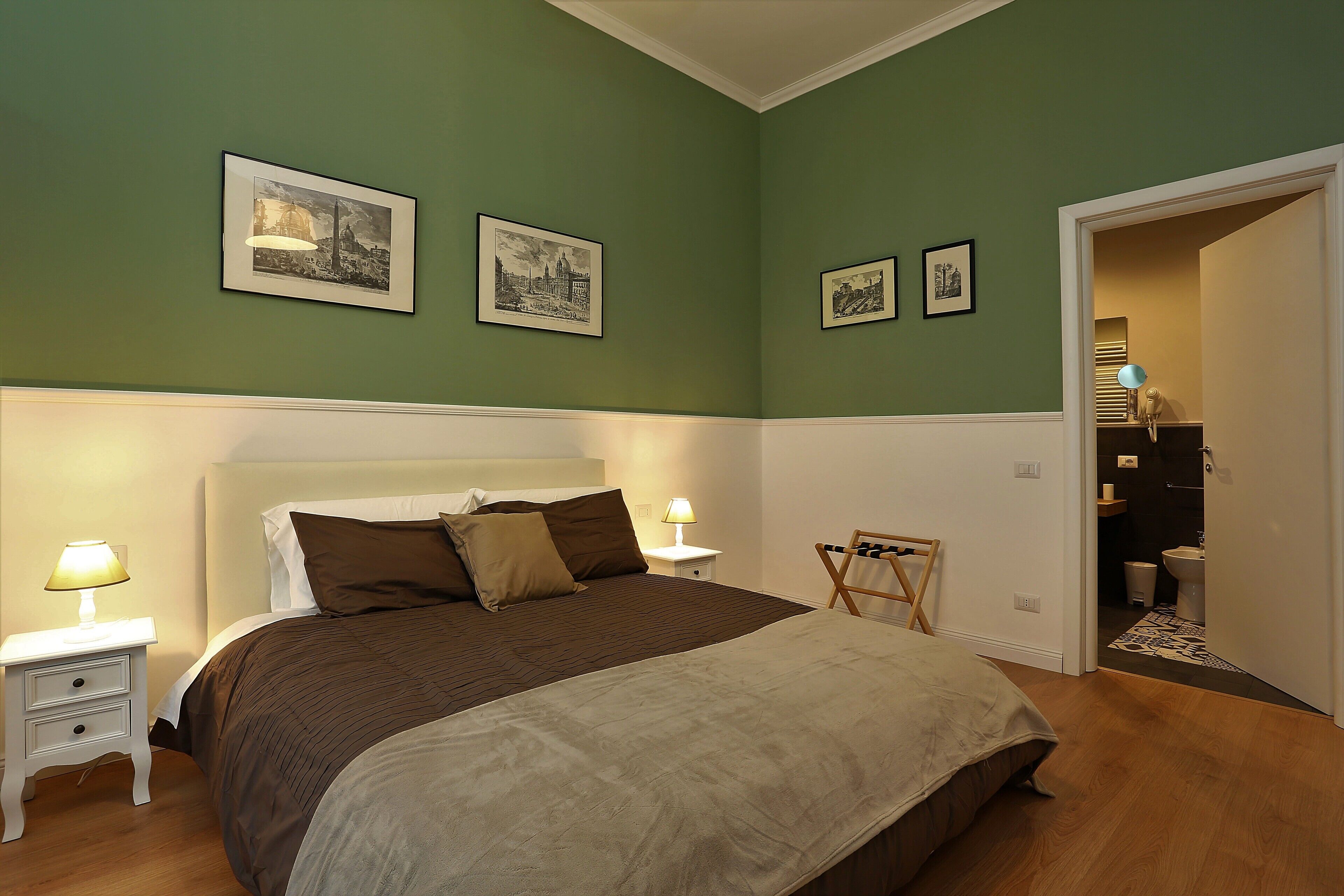 A bedroom with a large bed, two bedside tables with lamps, and three framed pictures on the wall.