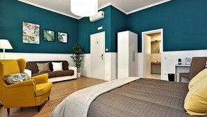 Ein modernes Hotelzimmer mit türkisfarbenen Wänden, einem großen Bett, einem Schlafsofa, einem gelben Sessel und einem Schreibtisch mit Stuhl.