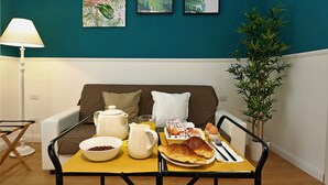 Ein Frühstücksarrangement mit einer Schüssel Müsli, einer Kanne, einem Croissant und einer Eierplatte auf einem gelben Tisch in einem Raum mit türkisblauen Wänden und einem weißen Sofa.