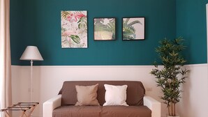 Ein Wohnzimmer mit türkisfarbenen Wänden, einem weißen Sofa mit braunen Kissen und drei gerahmten Pflanzenbildern.