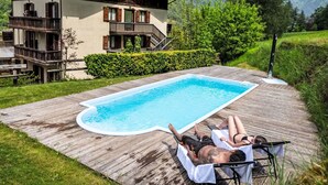 A wooden deck with a swimming pool, a two-story chalet, and a mountainous backdrop. - Nice apartment with pool, WIFI, TV, terrace, pets allowed, panoramic view, close to Riva Del Garda (Pieve Di Ledro)