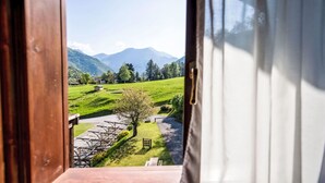 A view from a window of a room with a wooden door, overlooking a green field with a small building and mountains in the distance. - Nice apartment with pool, WIFI, TV, terrace, pets allowed, panoramic view, close to Riva Del Garda (Pieve Di Ledro)