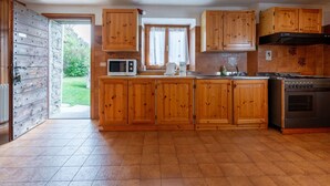 Een keuken met houten kastjes, een magnetron, een fornuis en een raam.