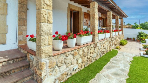 A stone building with a covered porch, potted red flowers, and a stone pathway. - Beautiful private villa for 8 people with WIFI, private pool, TV, terrace and panoramic view (Tordera)