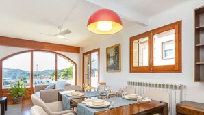 A dining area with a table set for four, a ceiling fan, and a large window with a view of the countryside. - Beautiful private villa for 8 people with WIFI, private pool, TV, terrace and panoramic view (Tordera)